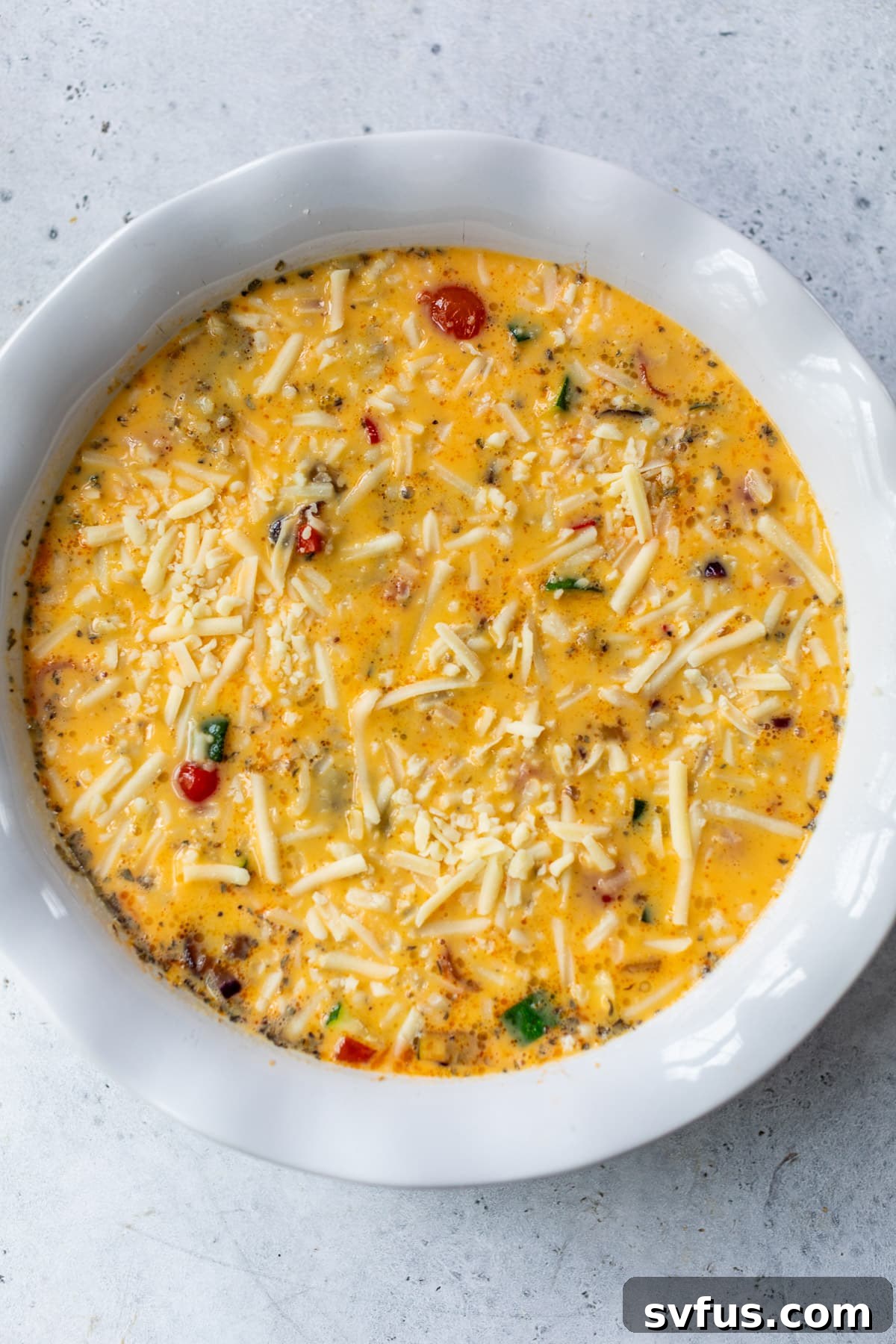 The liquid egg filling poured over sautéed vegetables and cheese in a large white pie plate, ready for baking.