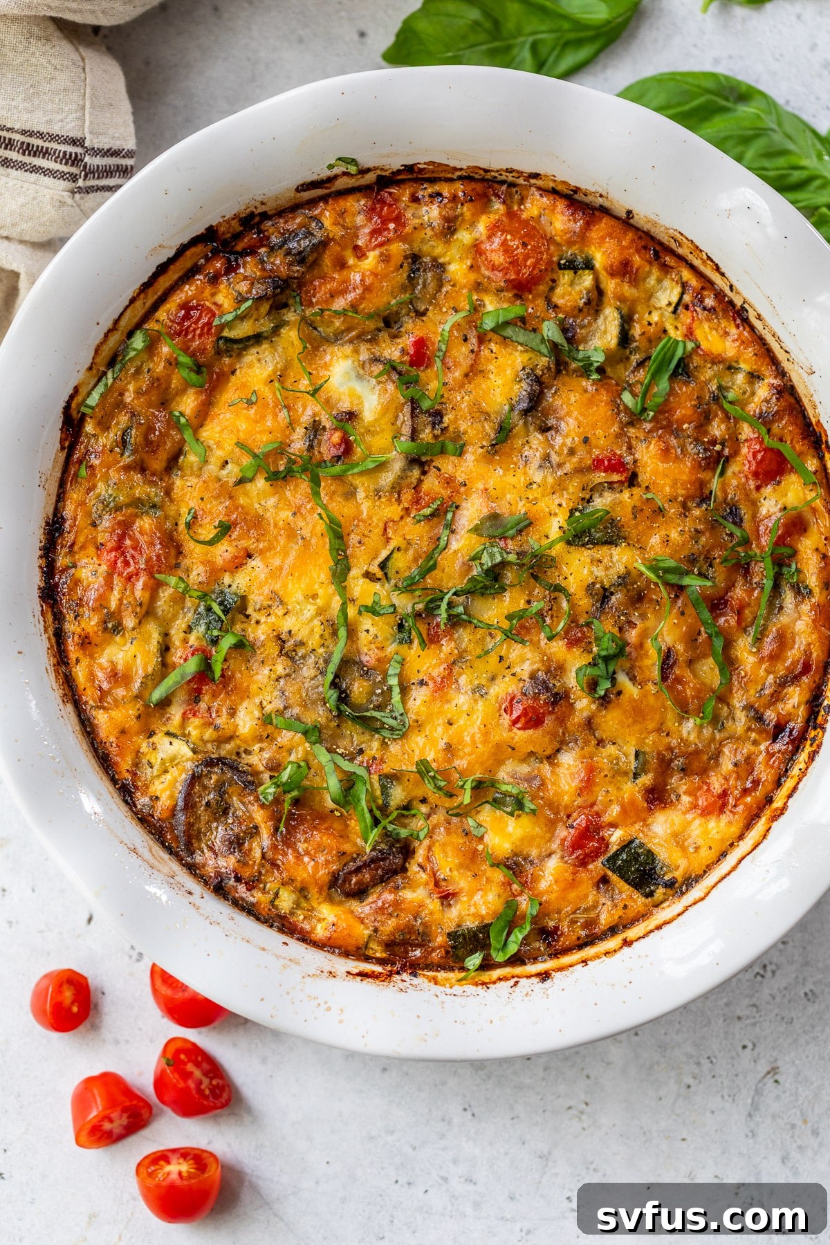 A perfectly baked crustless vegetable quiche in a large white pie plate, golden brown on top and edges.