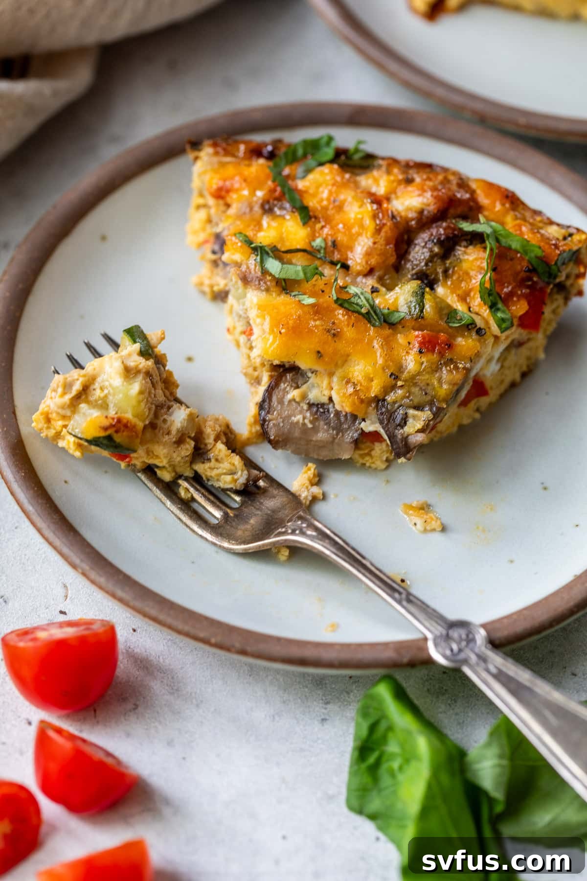 A fork taking a delicious bite out of a slice of crustless vegetable quiche on a white plate, showcasing the rich texture.
