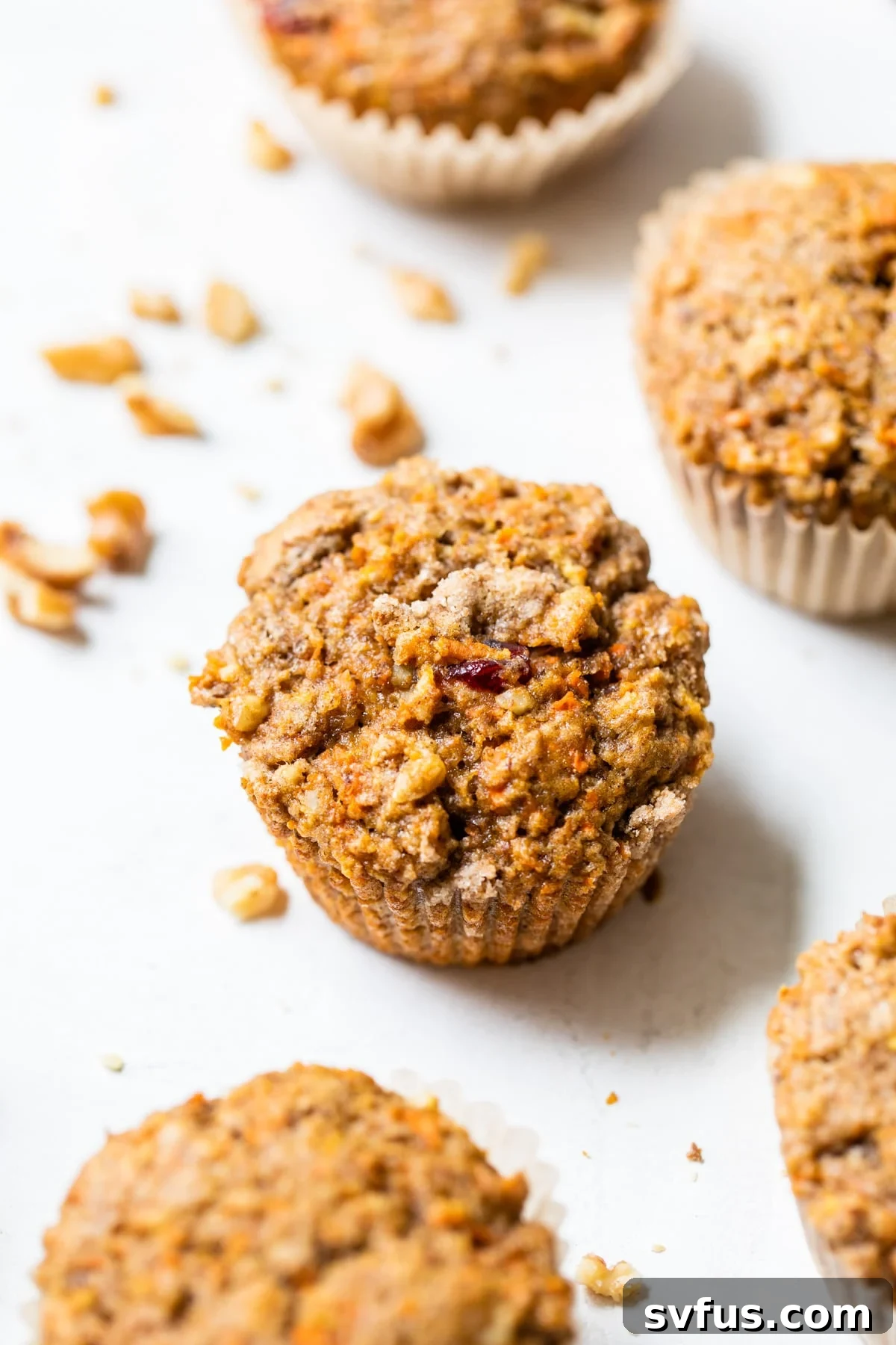 Freshly baked Vegan Morning Glory Muffins arranged on a rustic wooden table, with some muffins showing their golden-brown tops and visible specks of carrots and nuts.