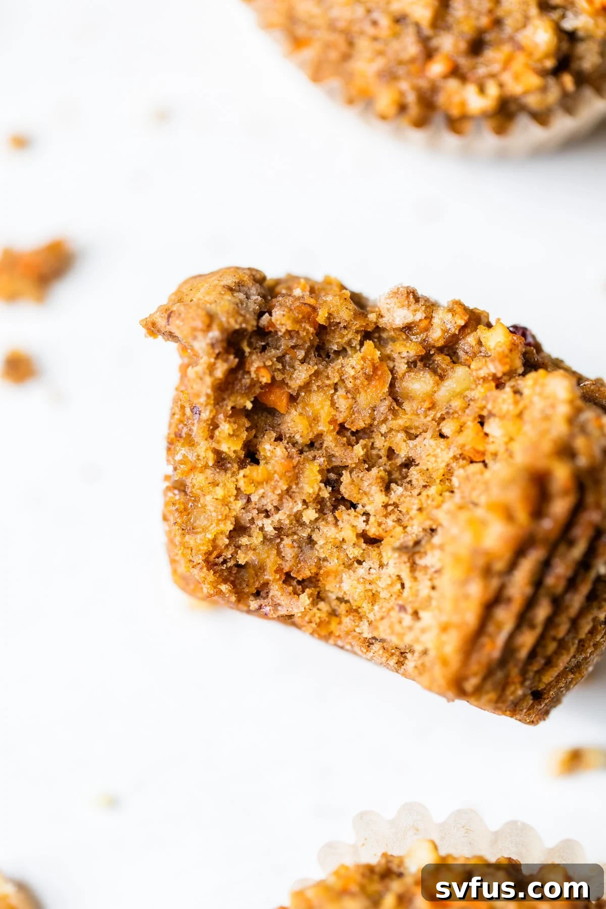 A close-up shot of a Vegan Morning Glory Muffin with a bite taken out, revealing the wholesome texture and visible chunks of fruit and nuts.