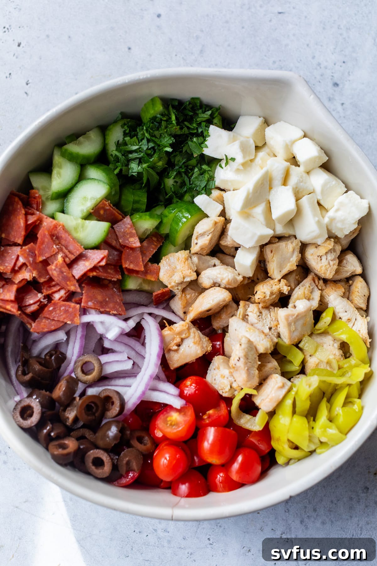 Büyük beyaz bir kasede İtalyan makarna salatası için etler, peynirler ve sebzeler.
