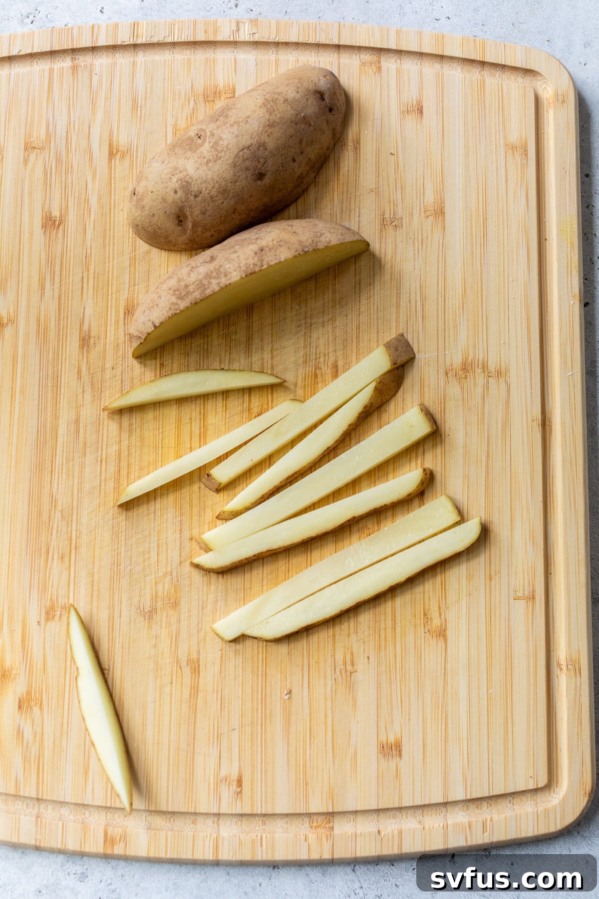 A person is carefully slicing russet potatoes into uniform french fry sticks, demonstrating the preparation step.