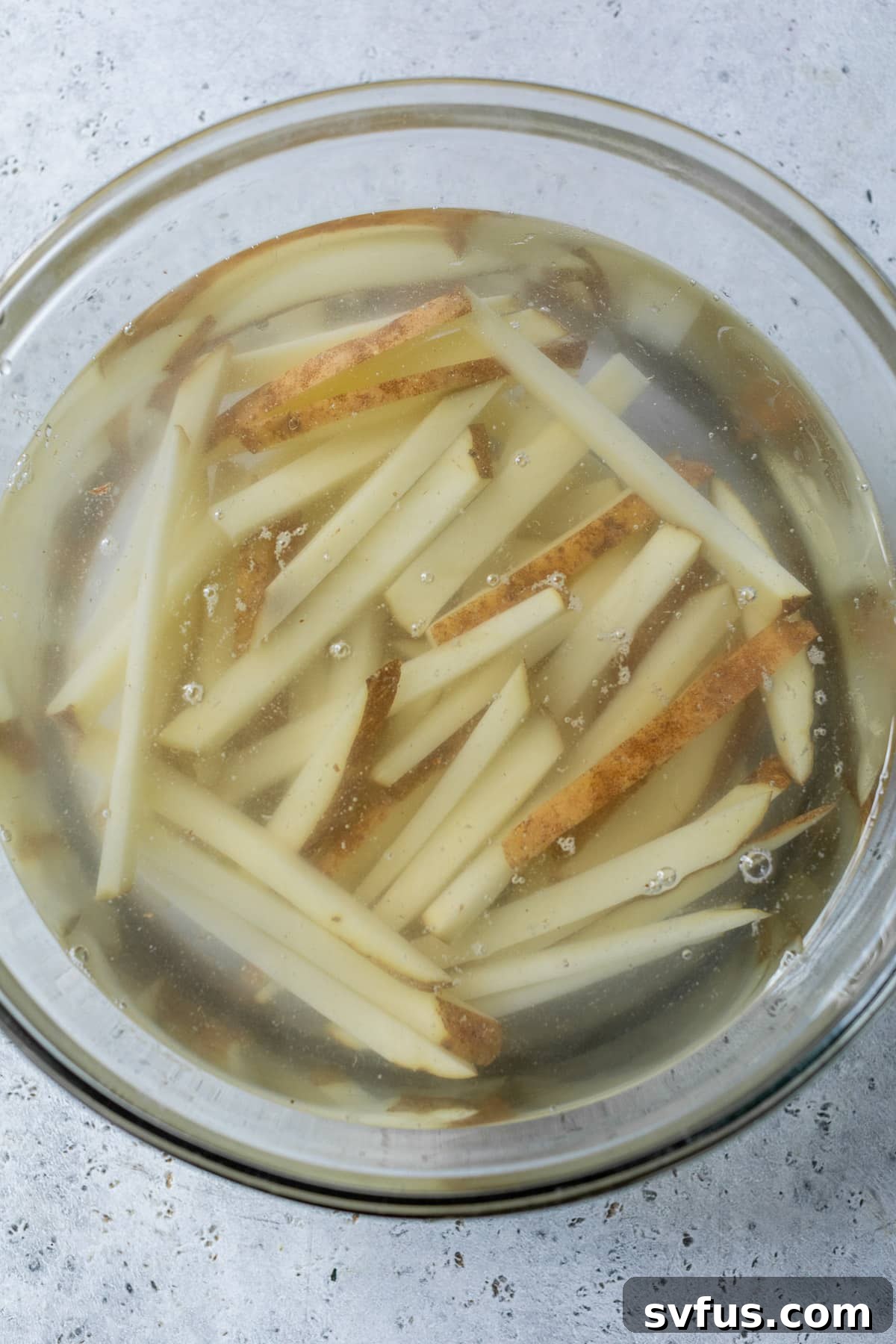 Raw french fries soaking in a bowl of cold water to remove excess starch.