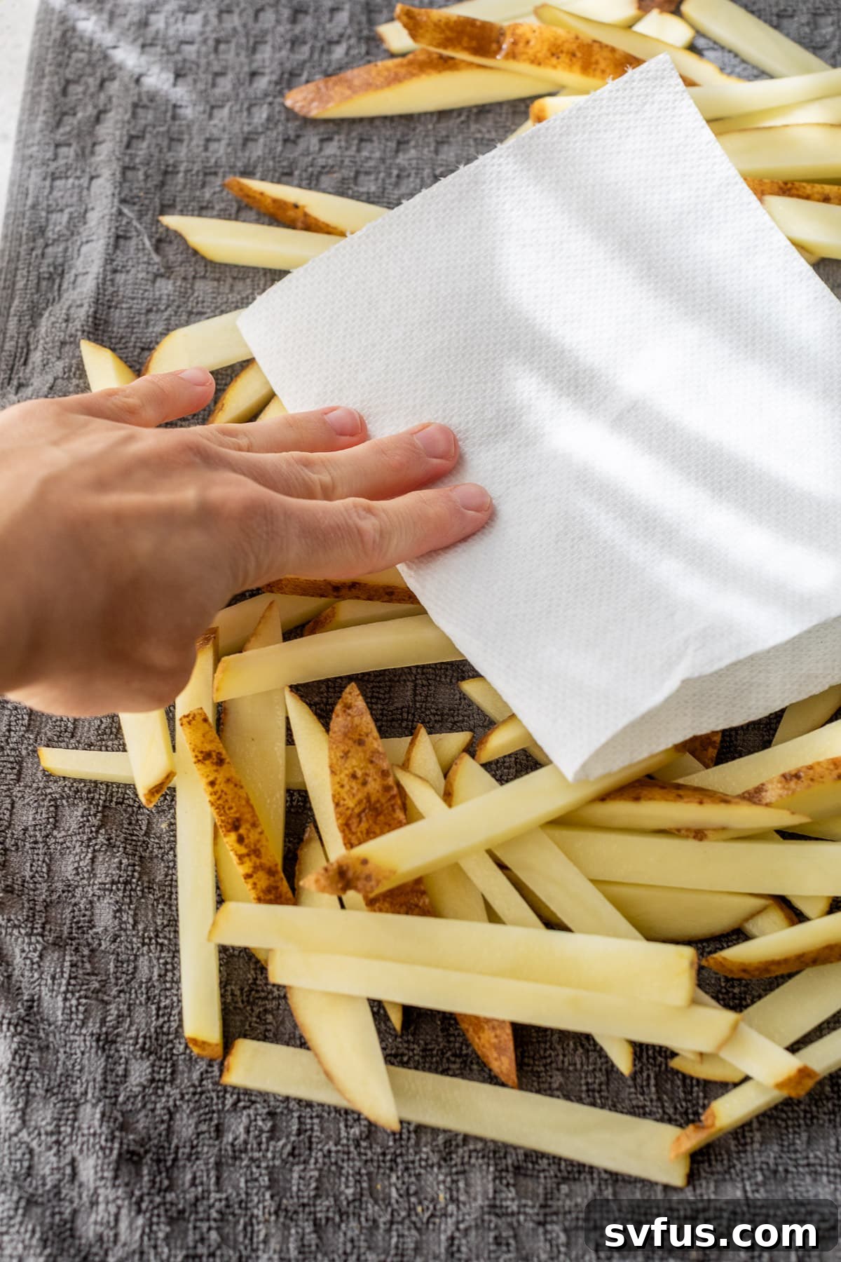 A woman's hand dabbing raw french fries with a paper towel, ensuring they are thoroughly dry before air frying.