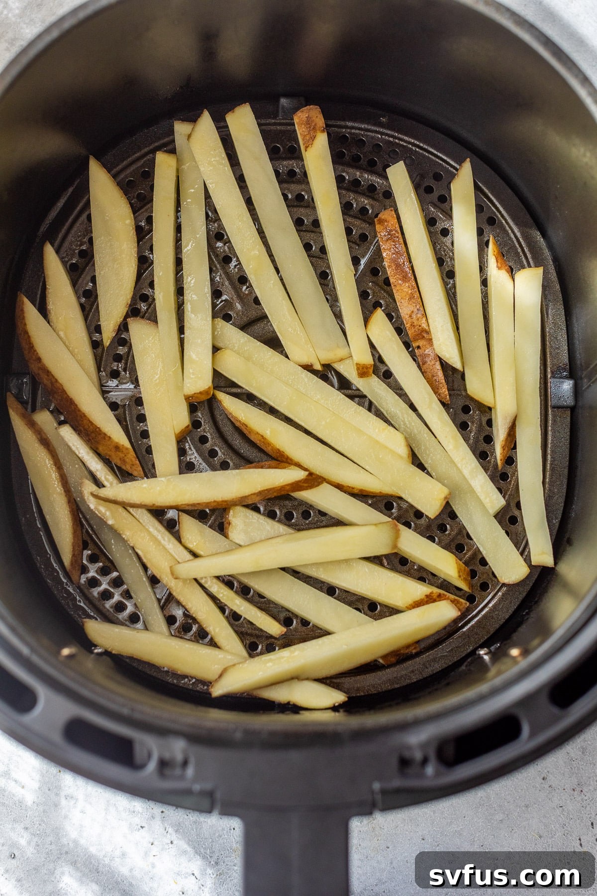 Raw french fries neatly arranged in a single layer inside an air fryer basket, ready for cooking.