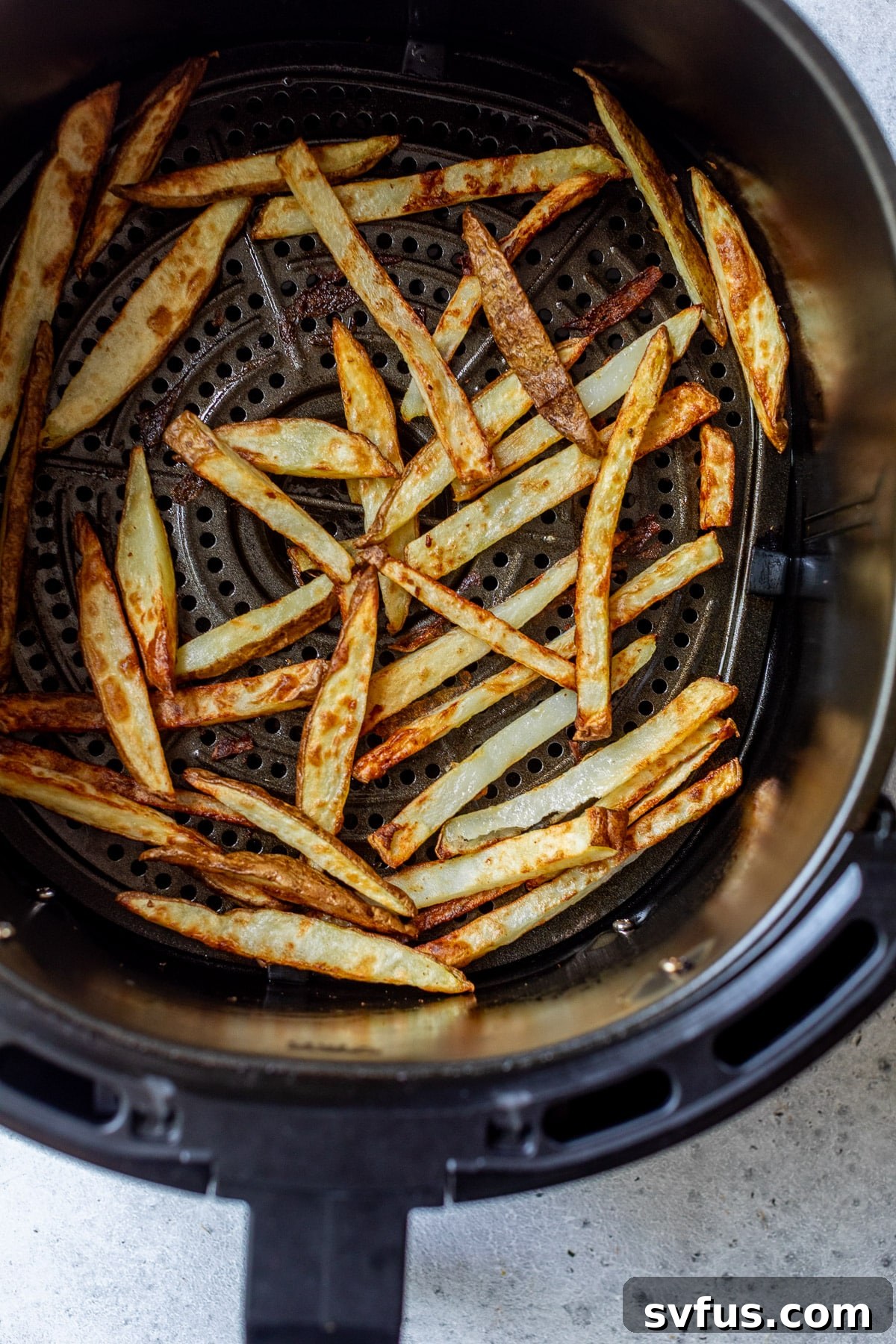 Perfectly cooked, golden-brown french fries filling an air fryer basket, showing the crispy result.