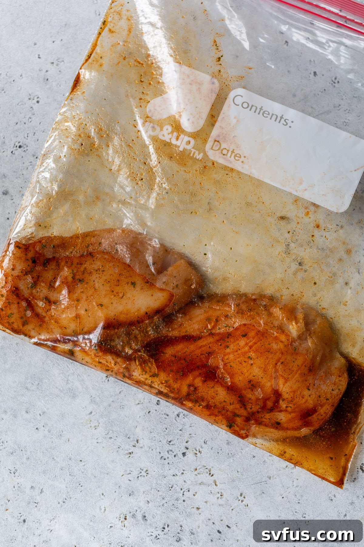 Two boneless chicken breasts marinating in a clear ziplock bag with a savory spice blend and olive oil, ensuring maximum flavor absorption.
