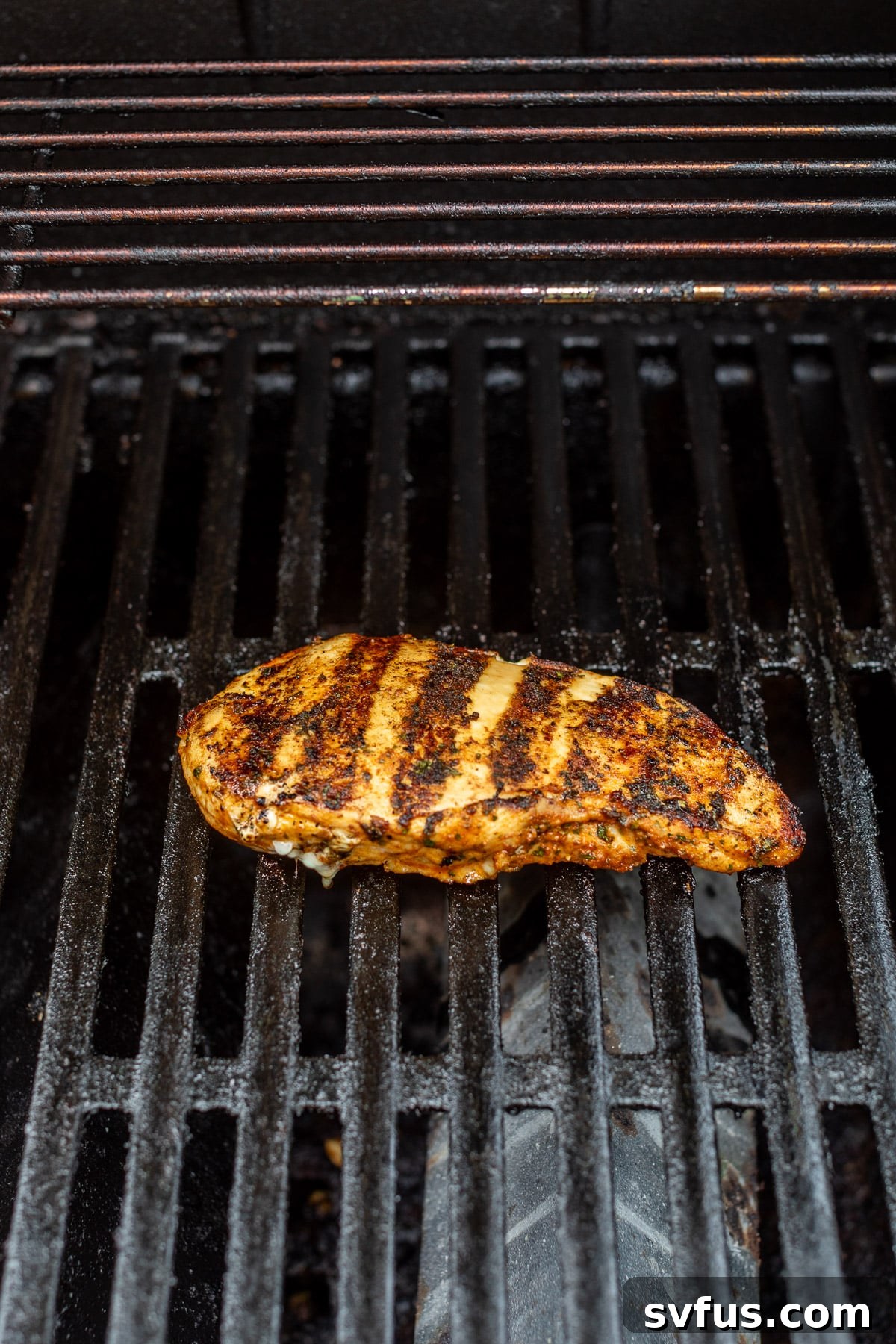 A chicken breast with distinct grill marks cooking on the grates of an outdoor grill, promising juicy flavor.