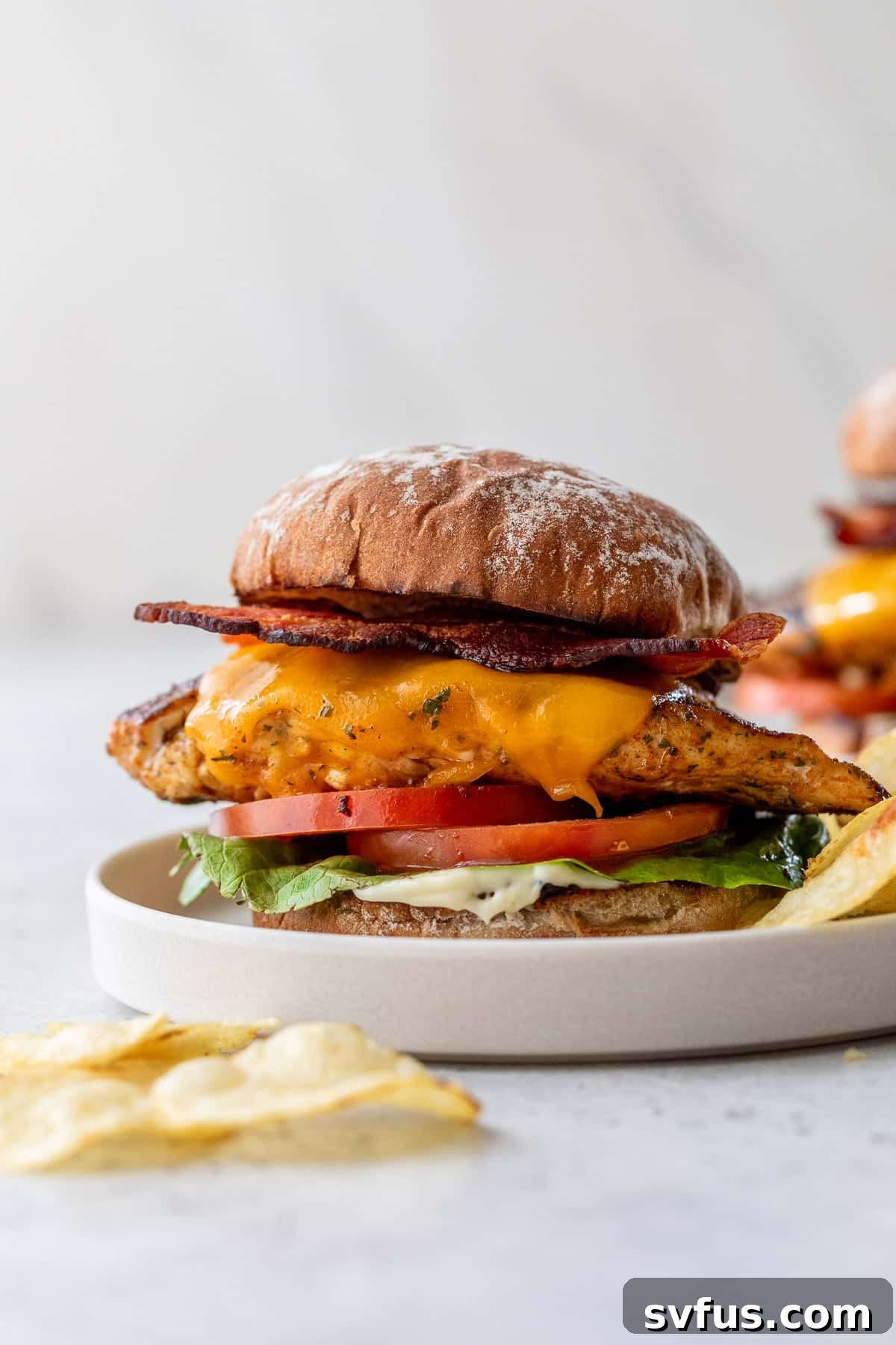 A close-up of an assembled Grilled Chicken Sandwich, showcasing the layers of grilled chicken, melted cheddar, crispy bacon, fresh tomato, and vibrant lettuce, presented on a white plate, inviting a delicious bite.