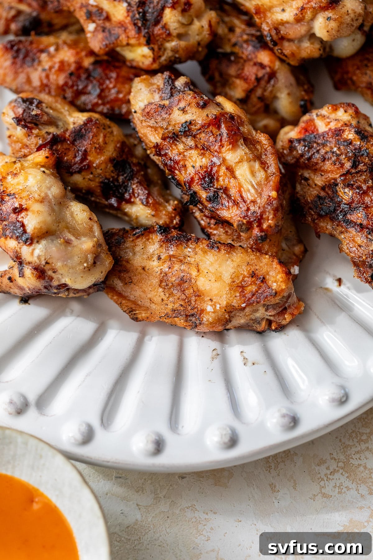 close up on a platter of grilled chicken wings with buffalo sauce on the side.