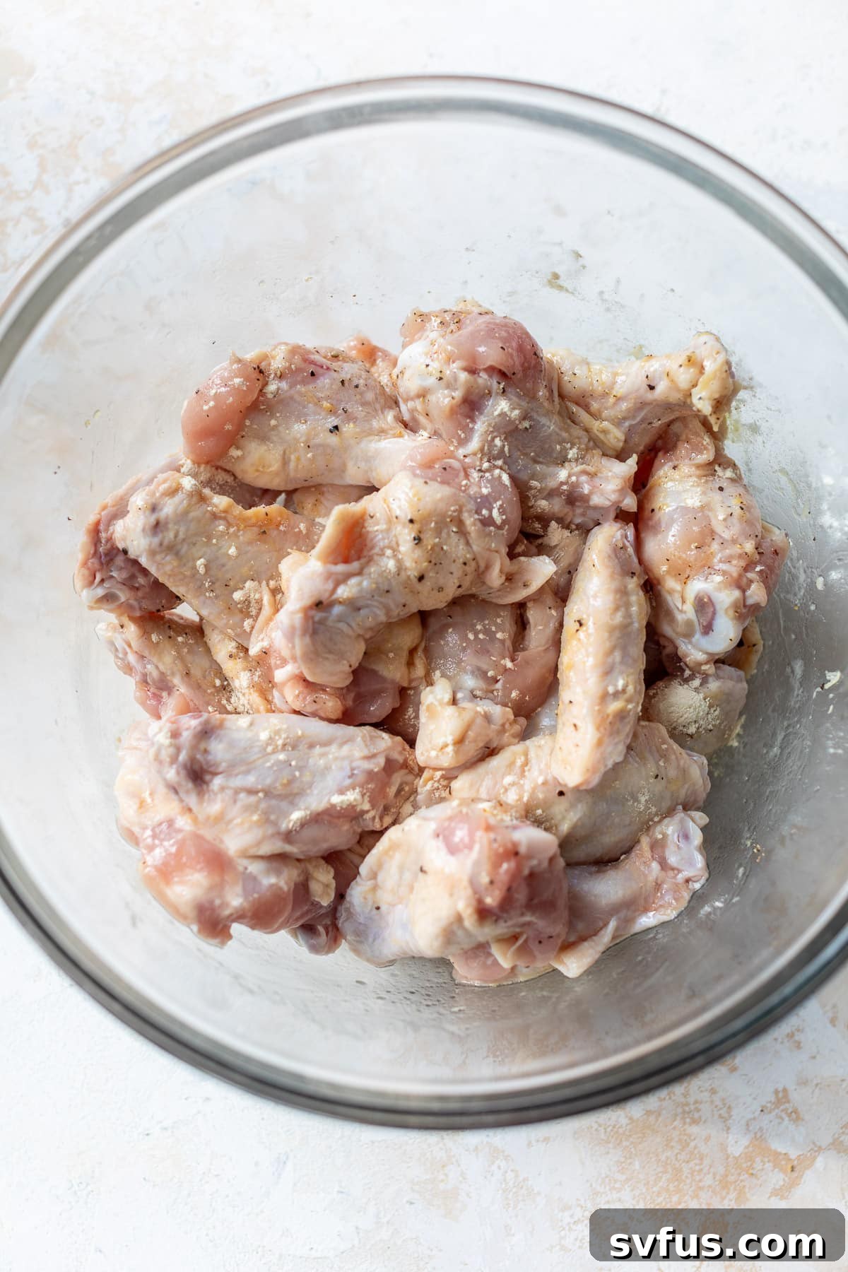 raw chicken wings with seasonings in a glass bowl.