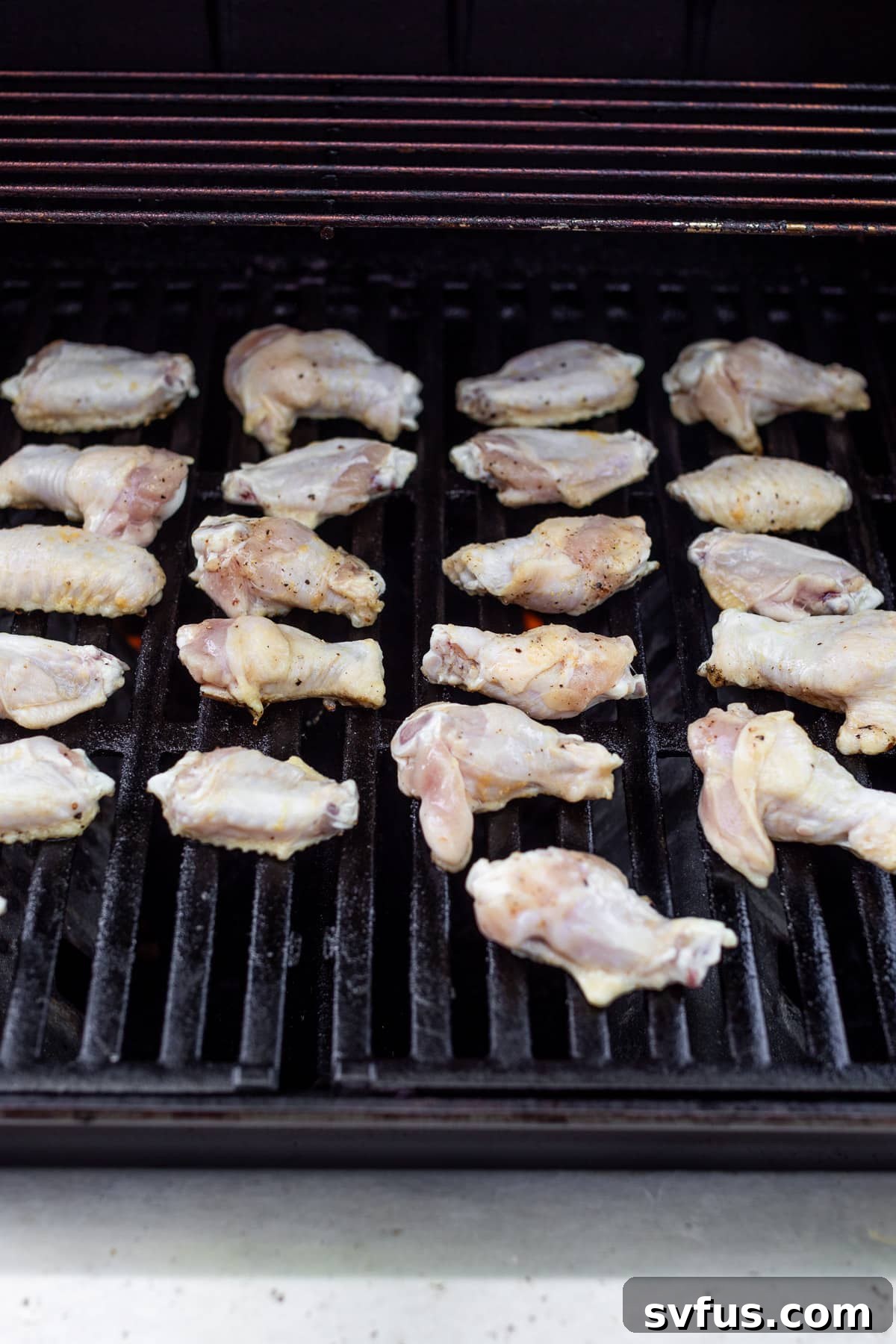 cooking rows of raw chicken wings on a grill.