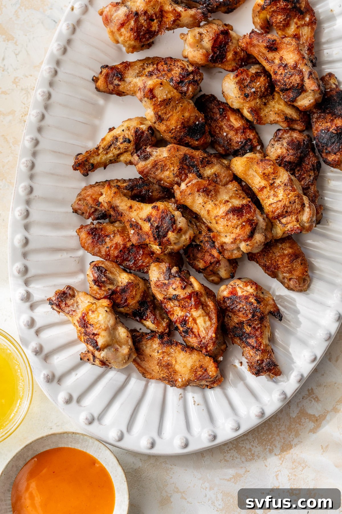 a platter of grilled chicken wings with buffalo sauce on the side.