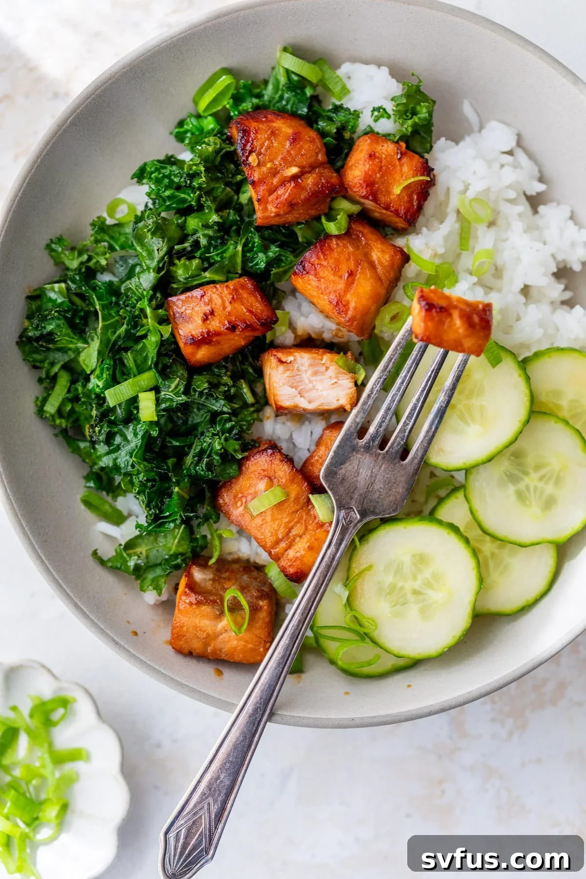 A fork lifts a perfectly cooked, golden-brown air fryer salmon bite from a colorful bowl filled with rice, fresh vegetables, and a sprinkle of green onion.