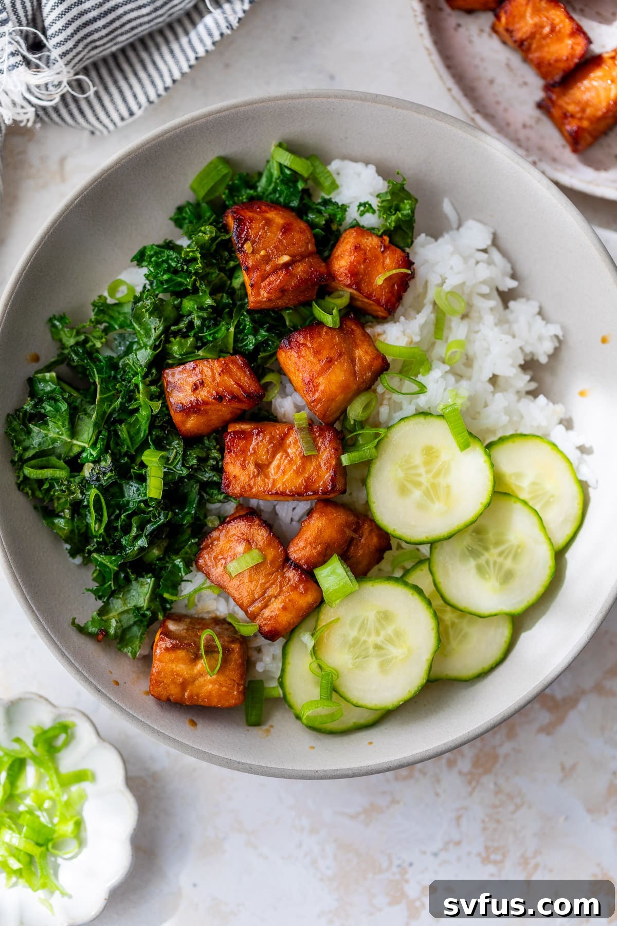 A vibrant bowl featuring air fryer salmon bites, crisp cucumber slices, fresh kale, and fluffy rice, creating a balanced and appealing meal.