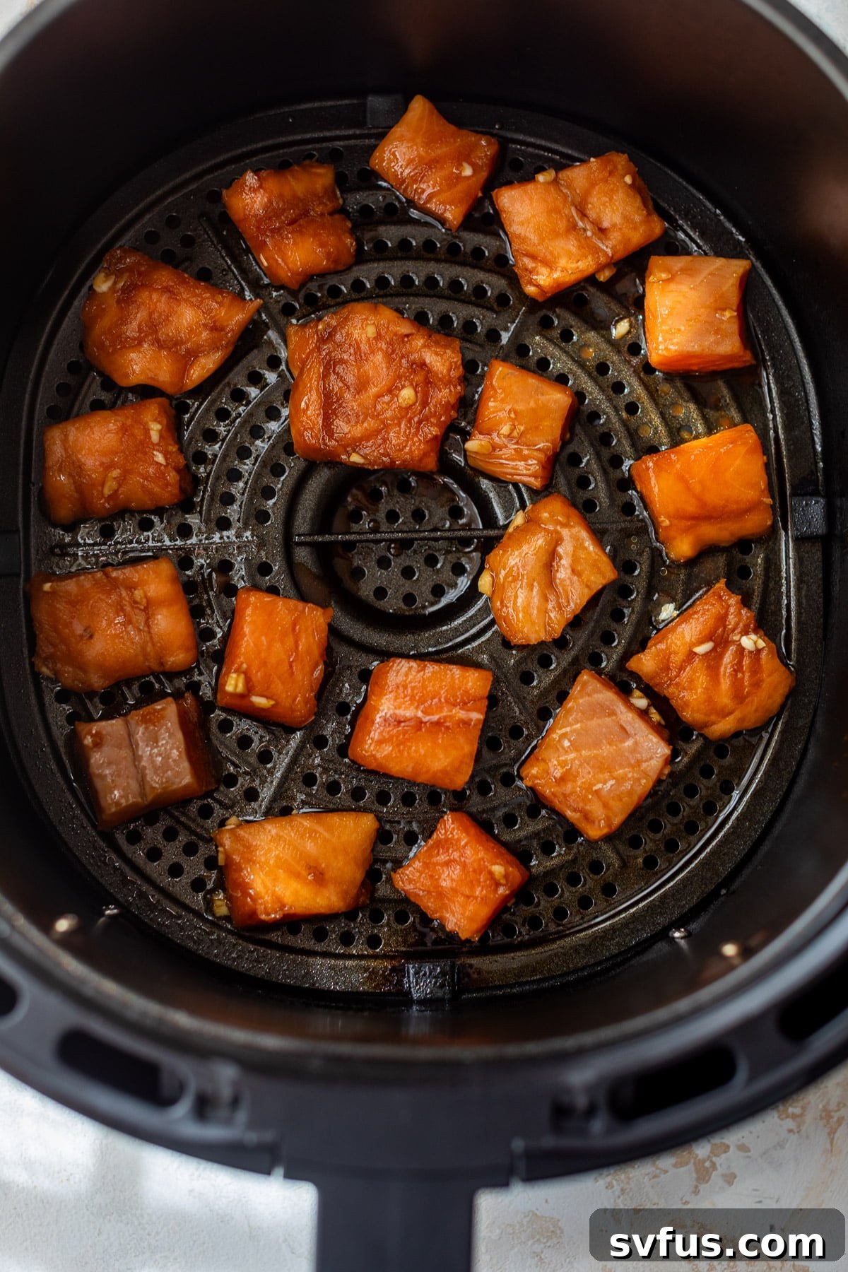 Uncooked, marinated salmon cubes arranged in a single layer inside an air fryer basket, ready for cooking.