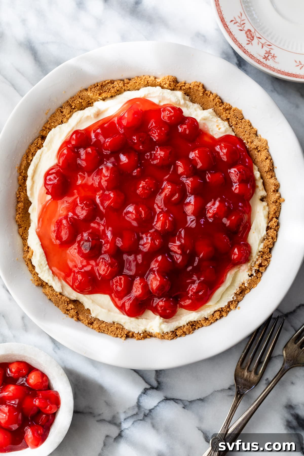 A whole cheesecake in a pie pan with a golden graham cracker crust and a smooth, creamy white filling, before the cherry topping is added.