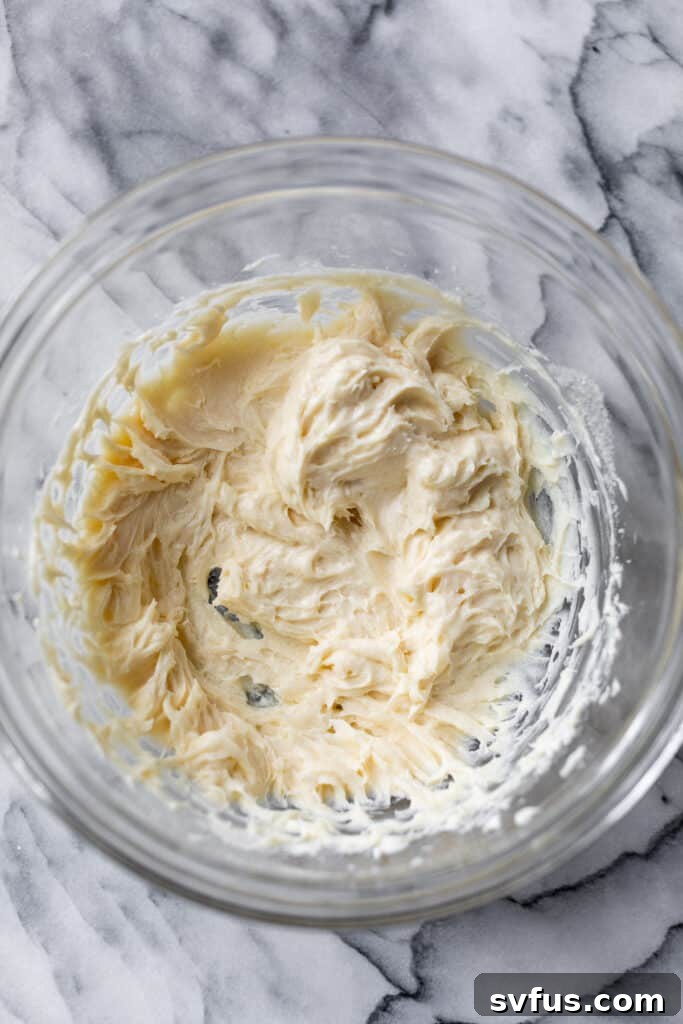 A large glass bowl filled with the smooth, creamy mixture of whipped cream cheese, powdered sugar, and vanilla extract.
