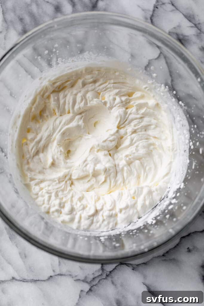 A large glass bowl filled with perfectly whipped heavy cream, showing distinct stiff peaks.