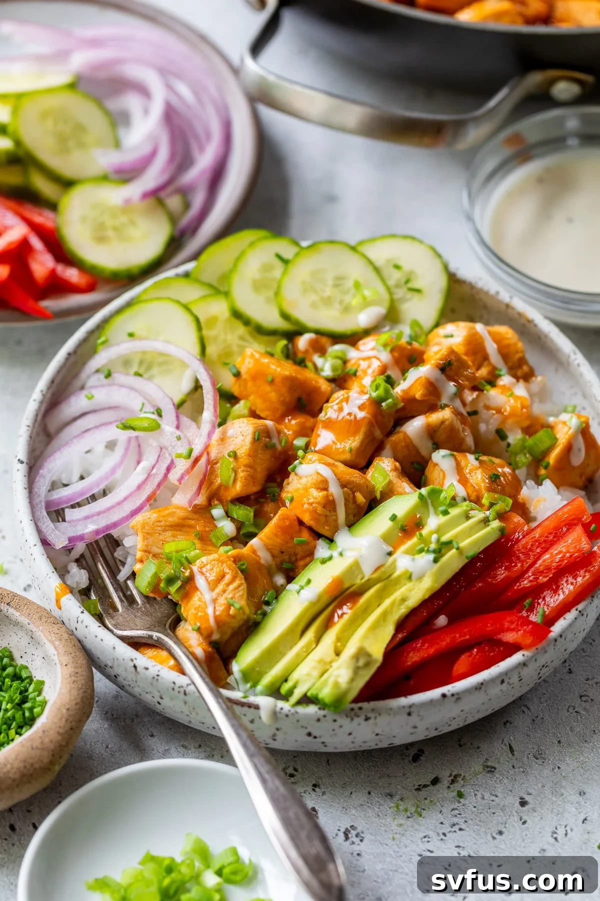 A close-up shot of a prepared Buffalo Chicken Bowl, garnished with fresh cucumber, red onion, and avocado, highlighting the vibrant colors and textures.