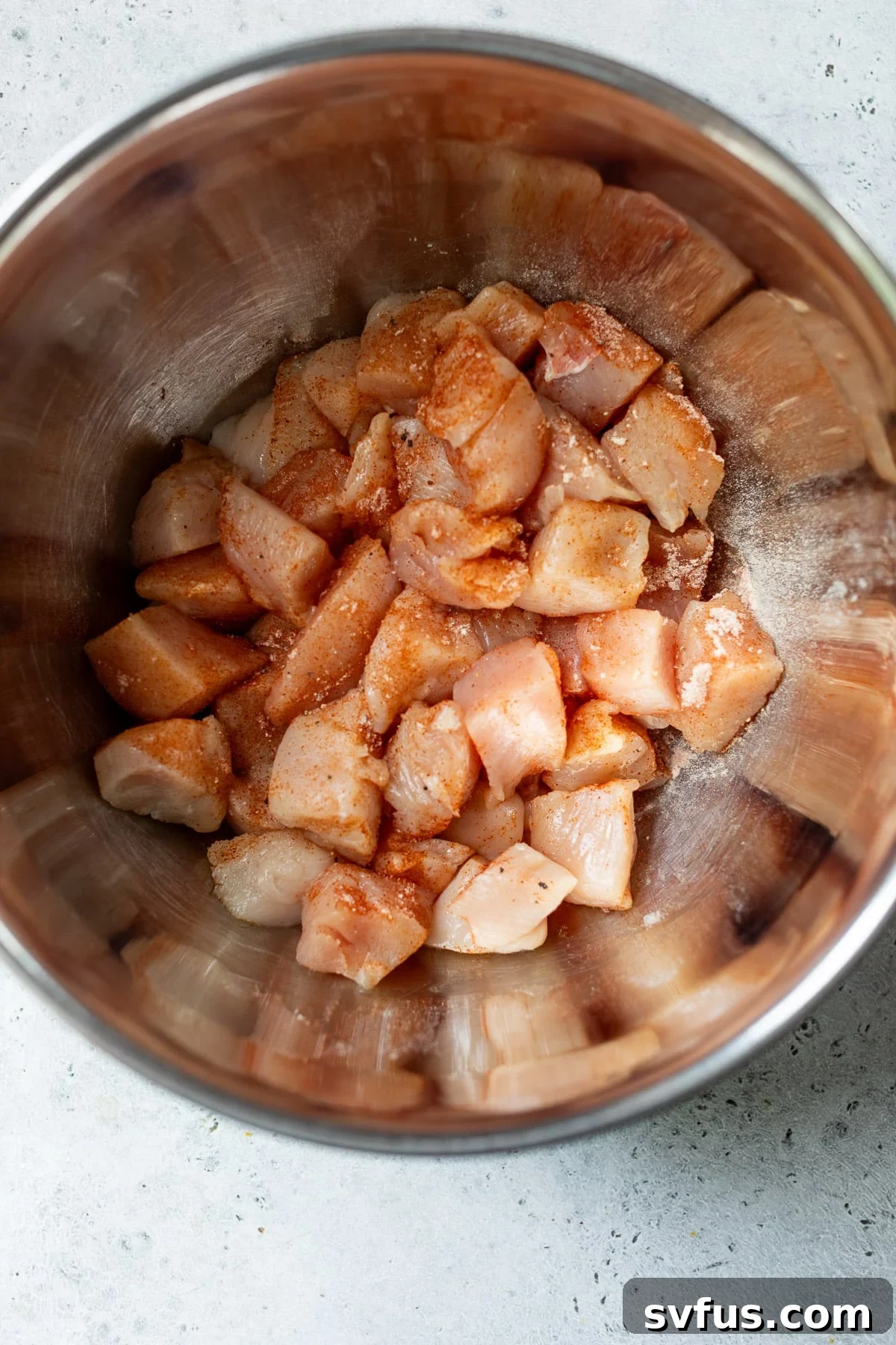 Diced chicken breast in a large bowl, evenly coated with a blend of savory seasonings, ready for searing.