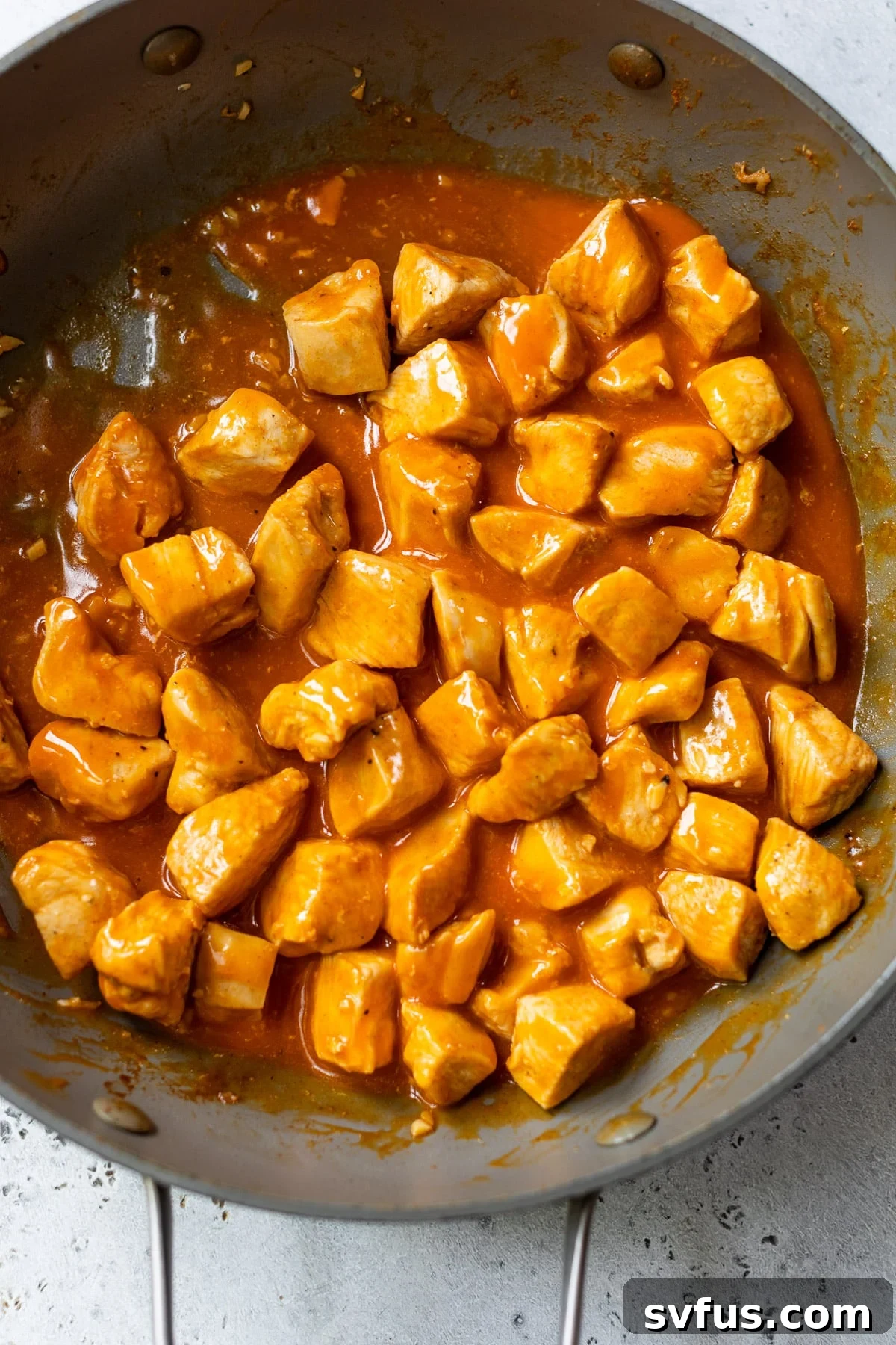 Diced chicken simmering in a rich, vibrant buffalo sauce within a skillet, ensuring every piece is coated.