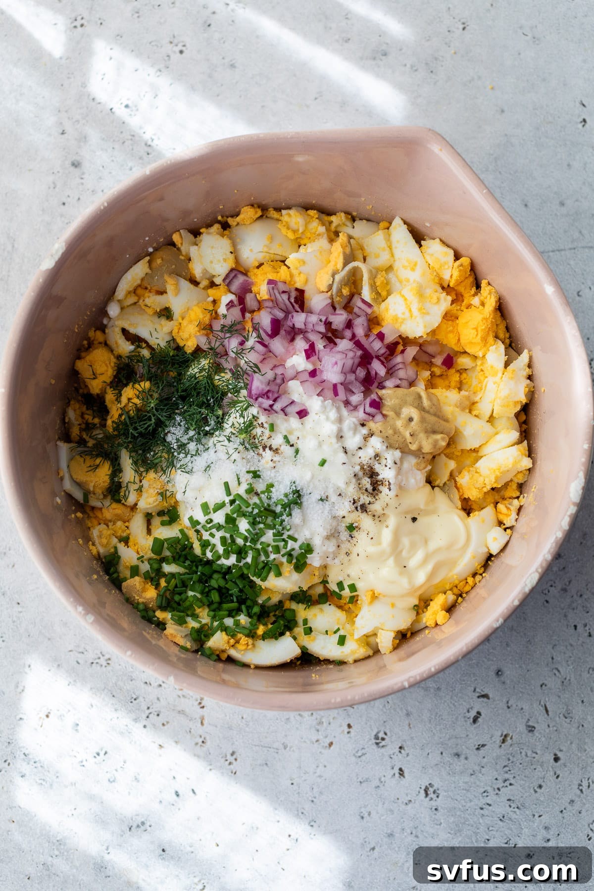 All the ingredients for Cottage Cheese Egg Salad, including cottage cheese, mayo, and herbs, mixed together in a large pink bowl before mashing.