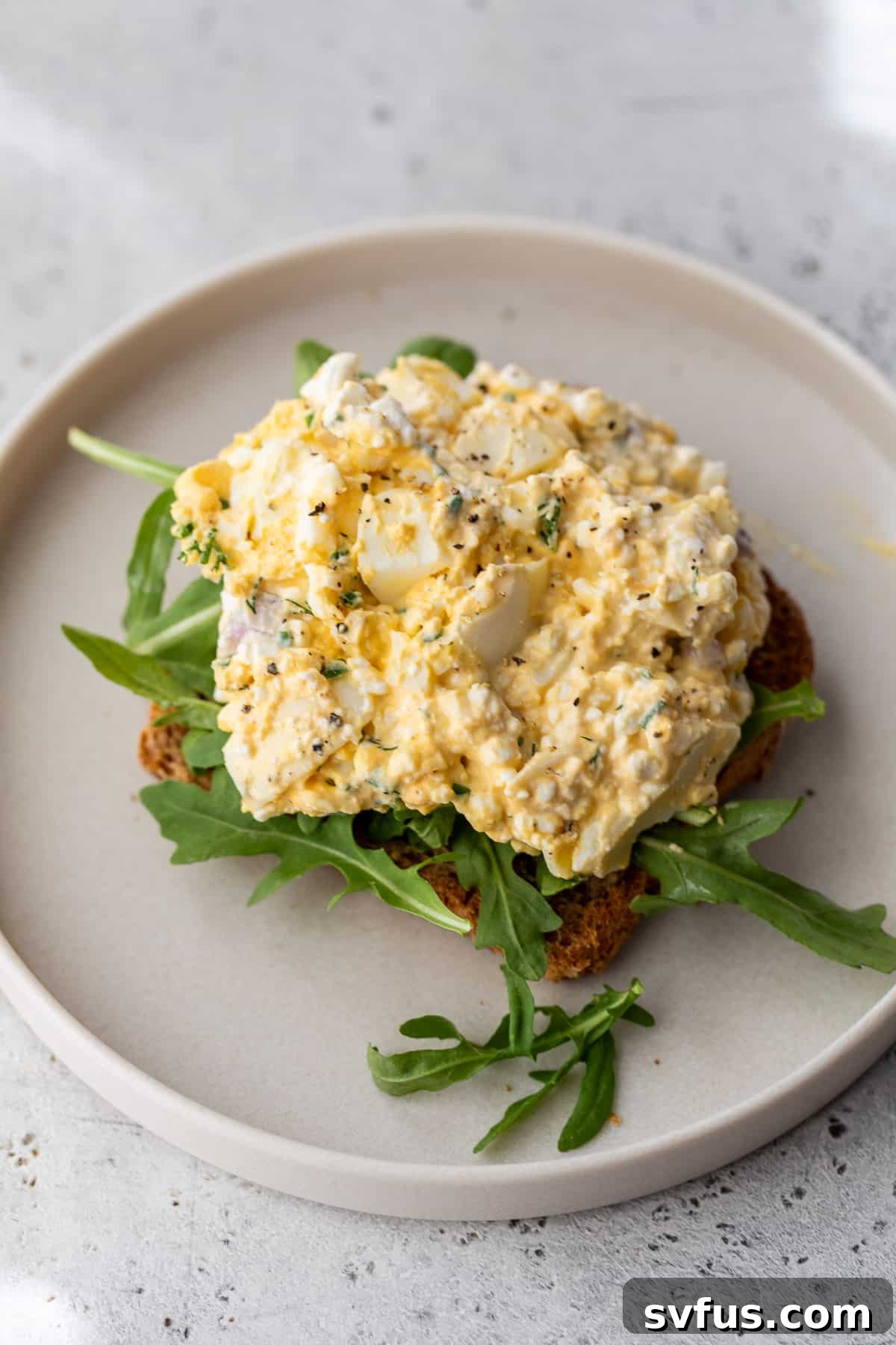 A slice of toast generously topped with Cottage Cheese Egg Salad and fresh arugula, presented on a plate.