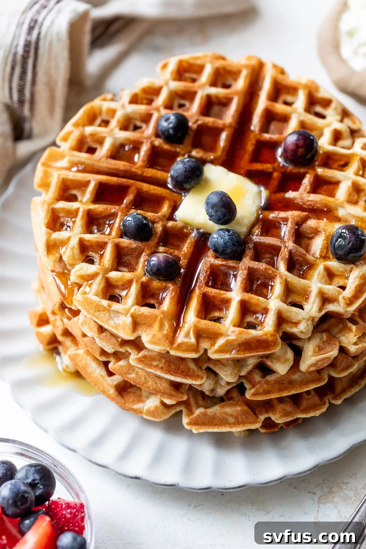 overhead view of a stack of protein waffles with butter, maple syrup, and blueberries on top.
