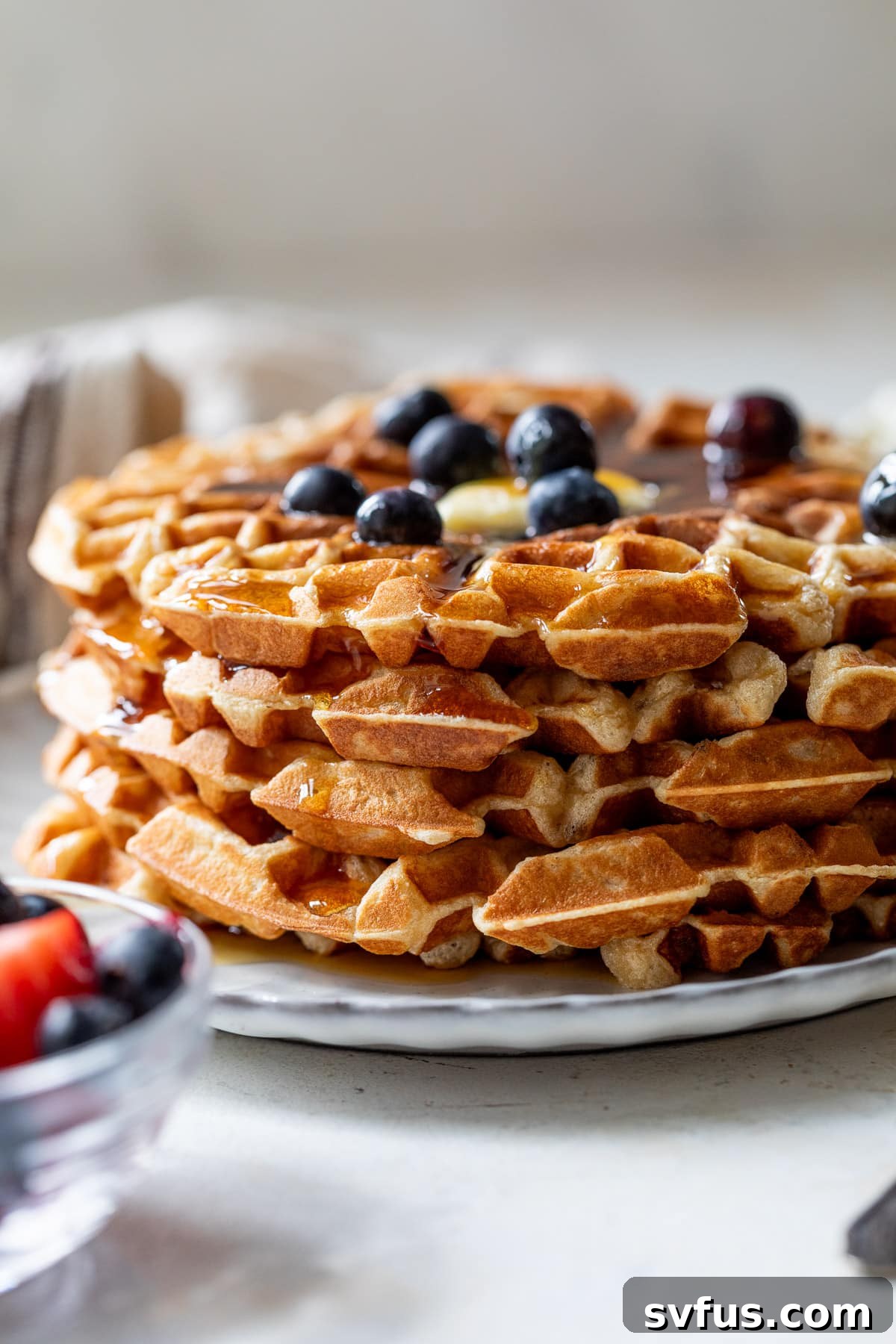 side view of a stack of protein waffles with butter, maple syrup, and blueberries on top.