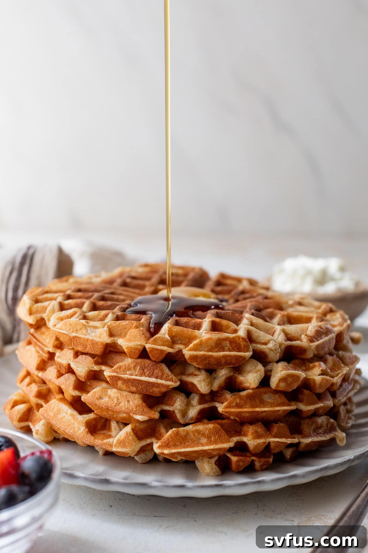 drizzling maple syrup over a stack of protein waffles.