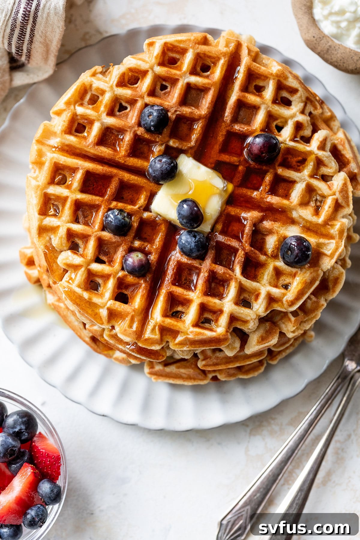 overhead view of a stack of protein waffles with butter, maple syrup, and blueberries on top.