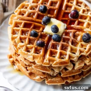 overhead view of a stack of protein waffles with butter, maple syrup, and blueberries on top.
