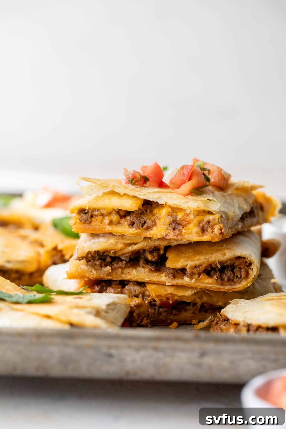 Close up on a stack of perfectly cooked sheet pan quesadillas topped with fresh salsa, indicating a delicious meal ready to be stored or enjoyed.