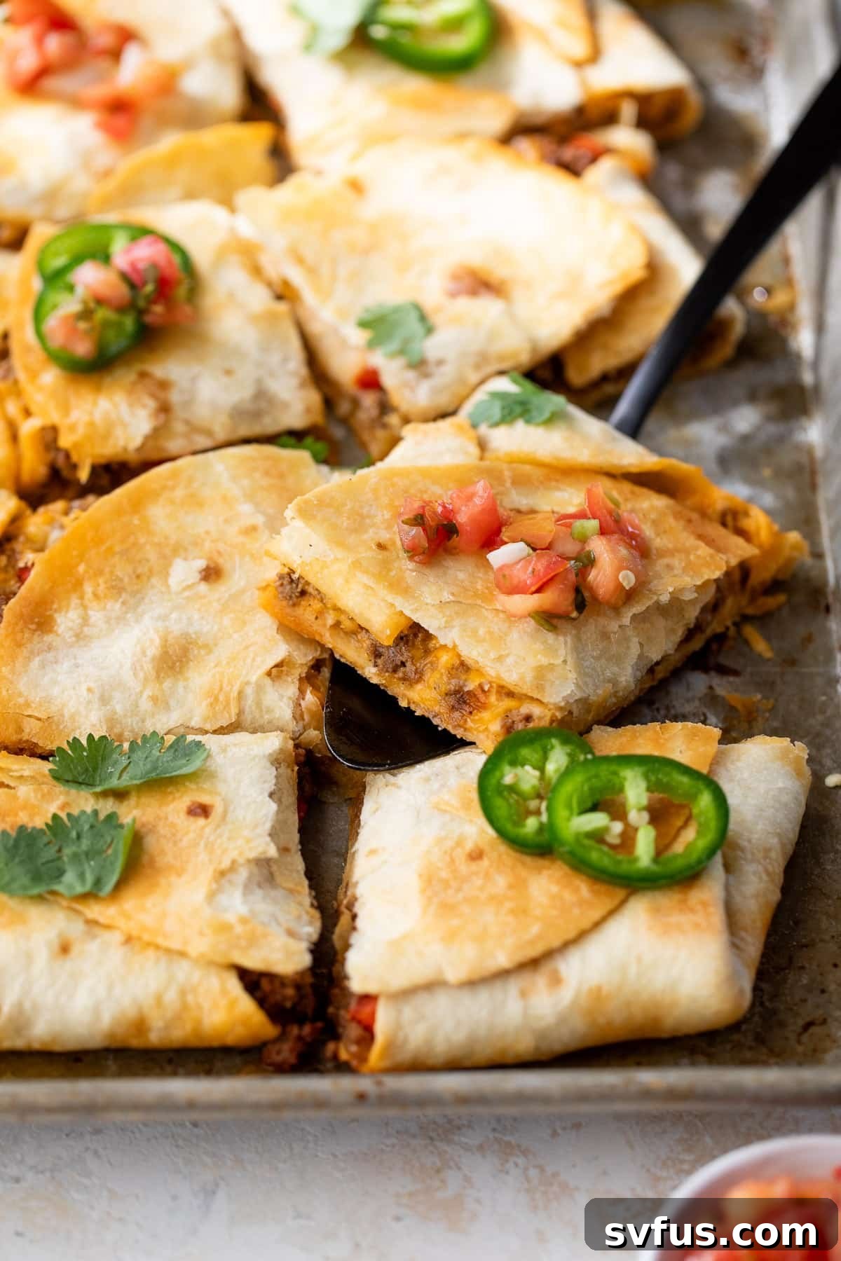 A spatula gently lifting a perfect slice of baked beef quesadilla from a large sheet pan, showcasing its crispy edges and melted cheese.