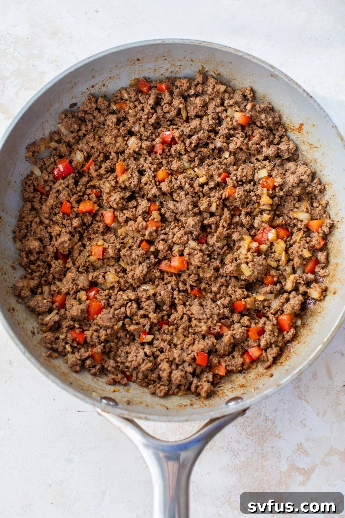 Overhead view of a savory ground beef, onion, bell pepper, and taco seasoning mixture cooking in a skillet, creating a rich filling.