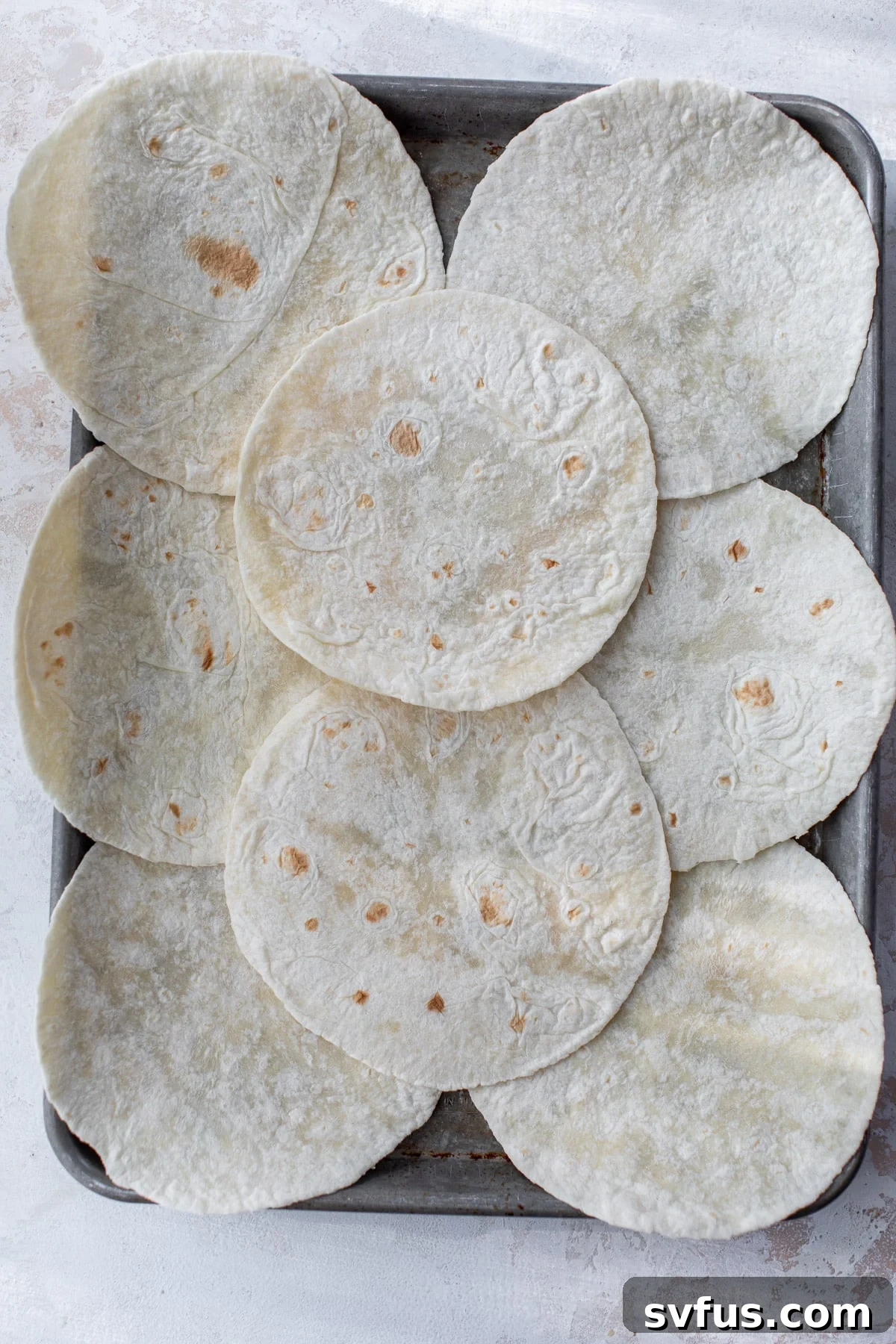 Flour tortillas carefully laid out on a sheet pan, forming the base for a large quesadilla, with some tortillas overhanging the edges.