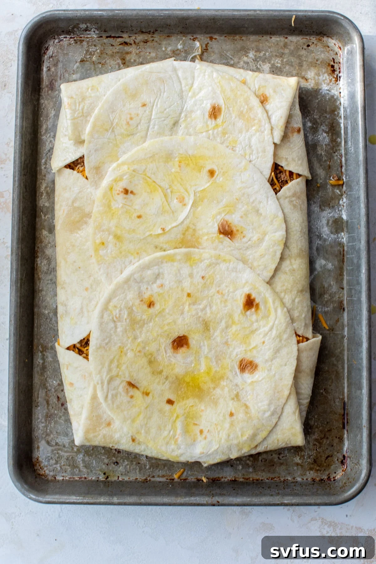 A large, fully assembled quesadilla on a sheet pan, with the outer tortillas folded over the filling and additional tortillas on top, ready for baking.