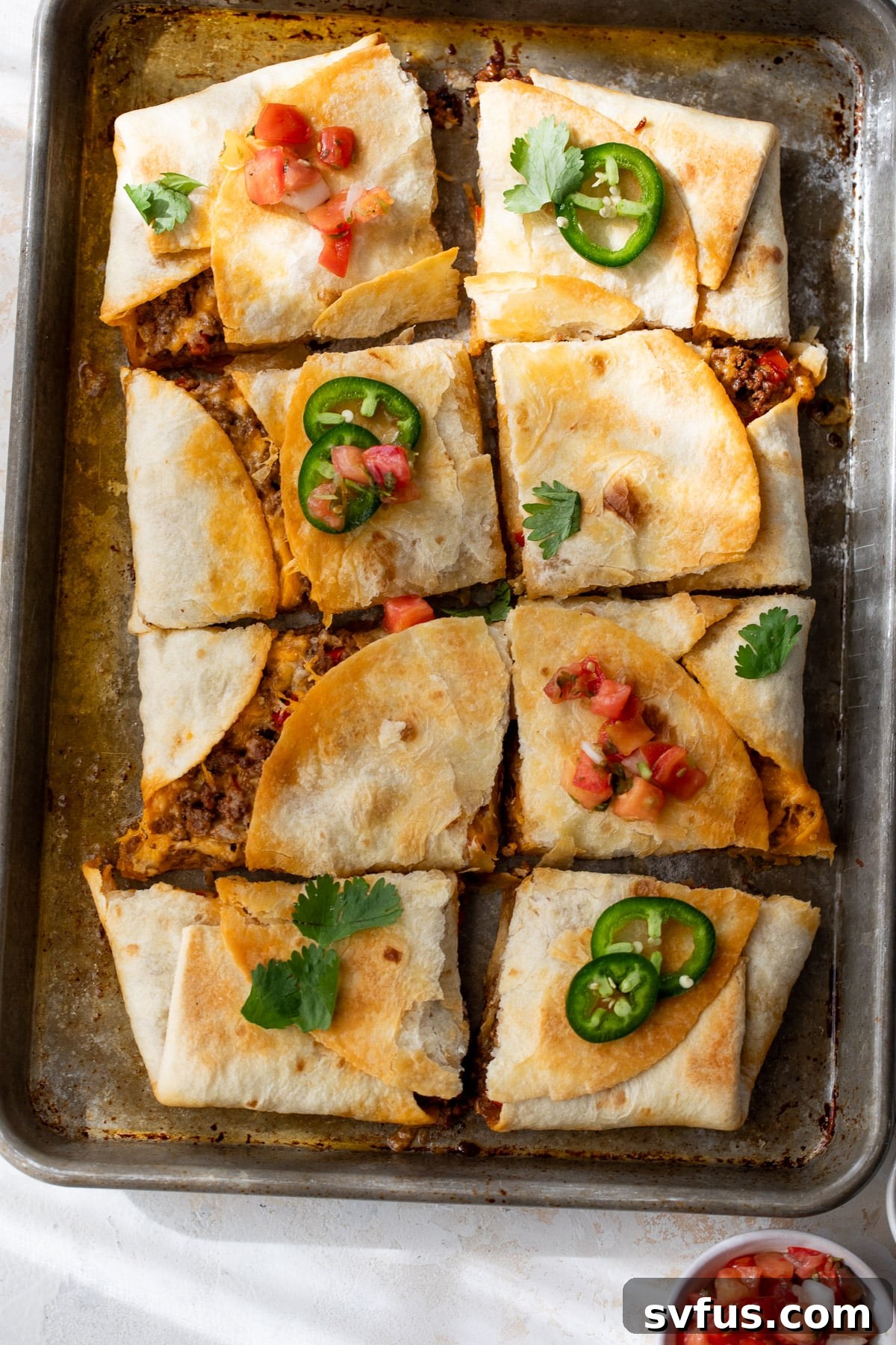 Sliced beef quesadillas on a sheet pan, adorned with vibrant jalapeños and fresh salsa, showcasing a tempting and ready-to-eat meal.