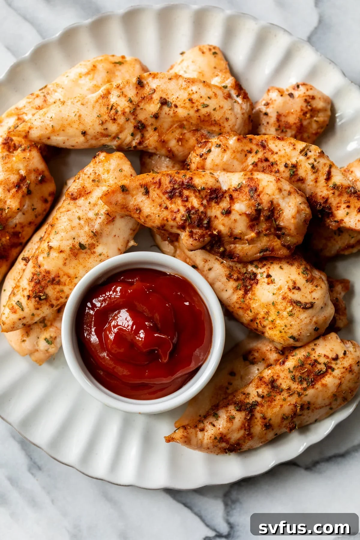 A vibrant pile of golden-brown baked chicken tenders served on a clean white plate, accompanied by a small ramekin of classic ketchup, inviting a delicious dip.