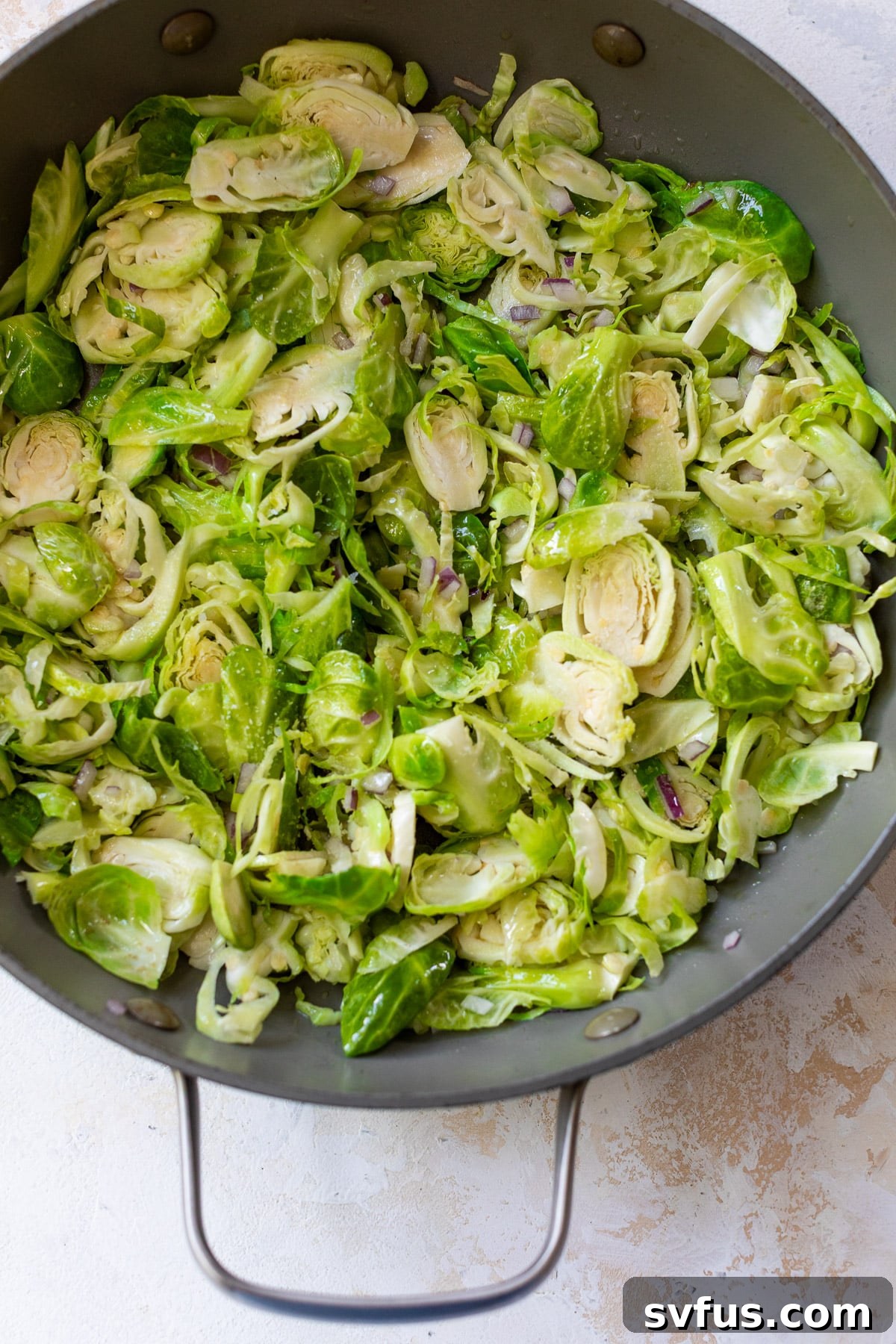 Shaved Brussels sprouts and diced red onion sizzling in olive oil in a large skillet, beginning to soften and brown.