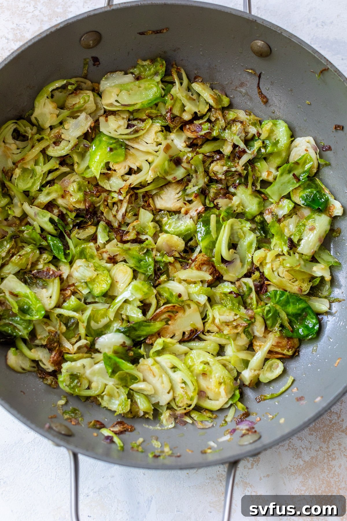 Sautéed shaved Brussels sprouts mixed with minced garlic in a hot skillet, developing a golden-brown color and tender texture.