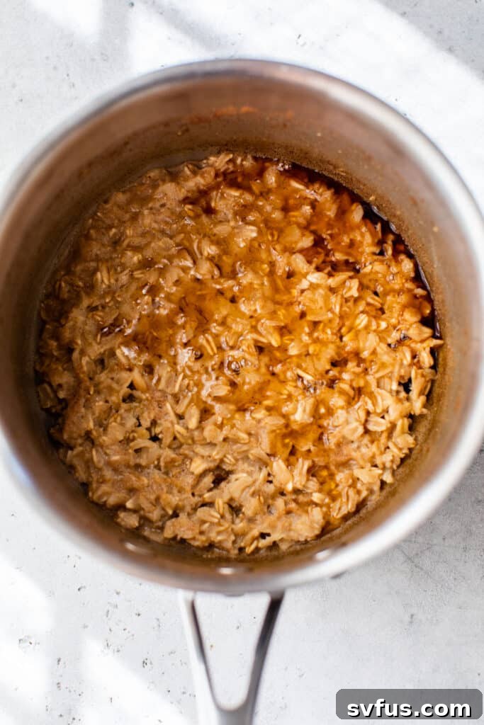 Cooked oatmeal in a small saucepan, freshly stirred with maple syrup and cinnamon, looking creamy and ready for apples.