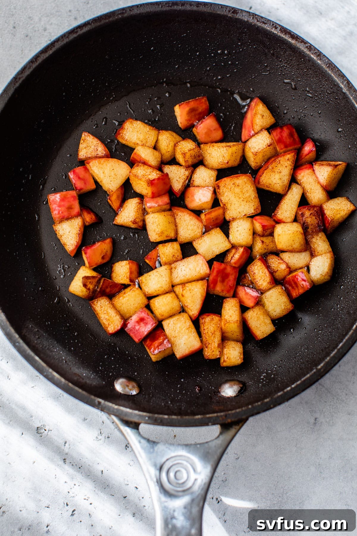 A skillet filled with diced, golden-brown cooked apples, perfectly spiced with cinnamon, ready to top oatmeal.