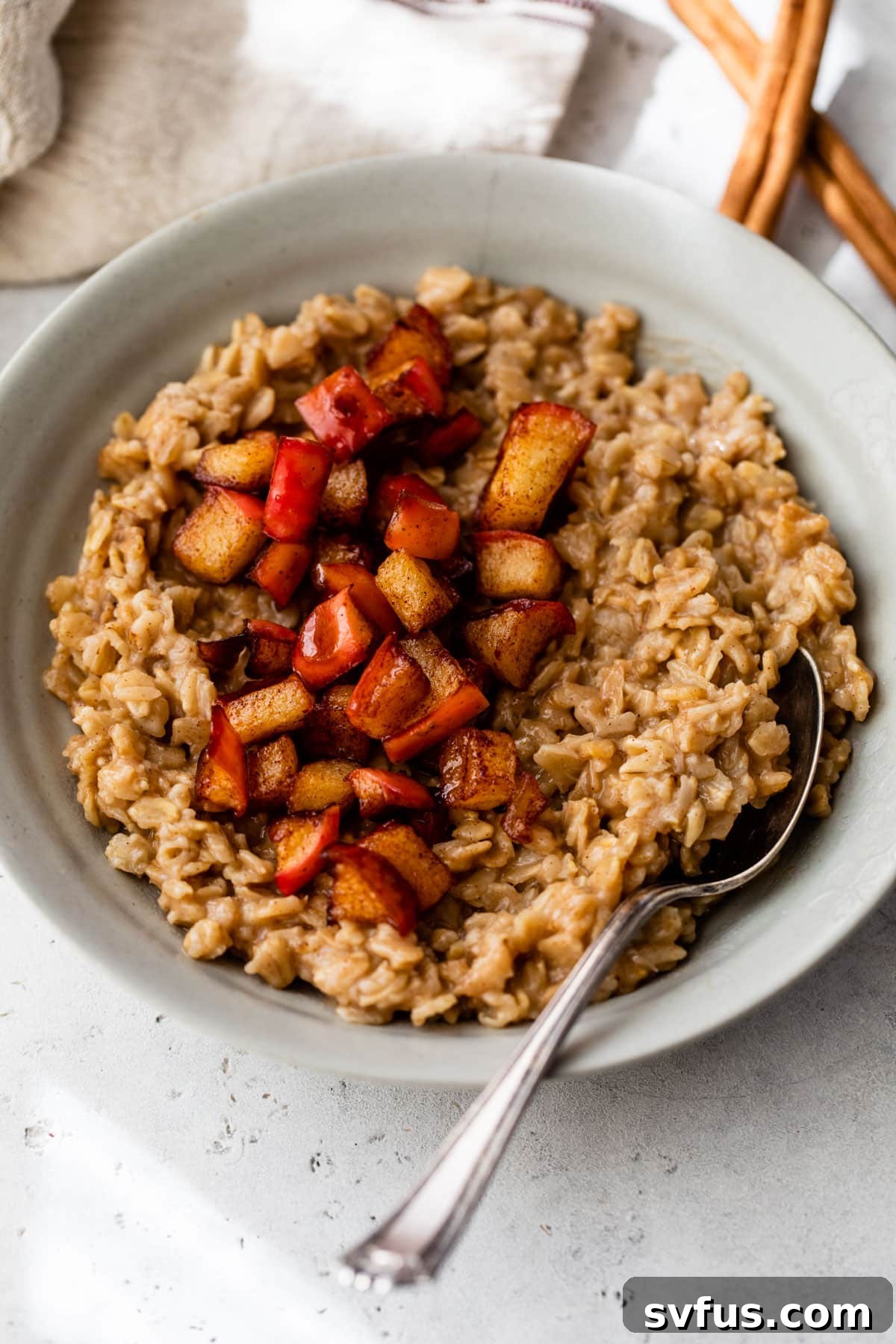 A gray-colored bowl with a spoon, generously filled with apple oatmeal, topped with more diced cooked apples, showcasing the delicious texture.