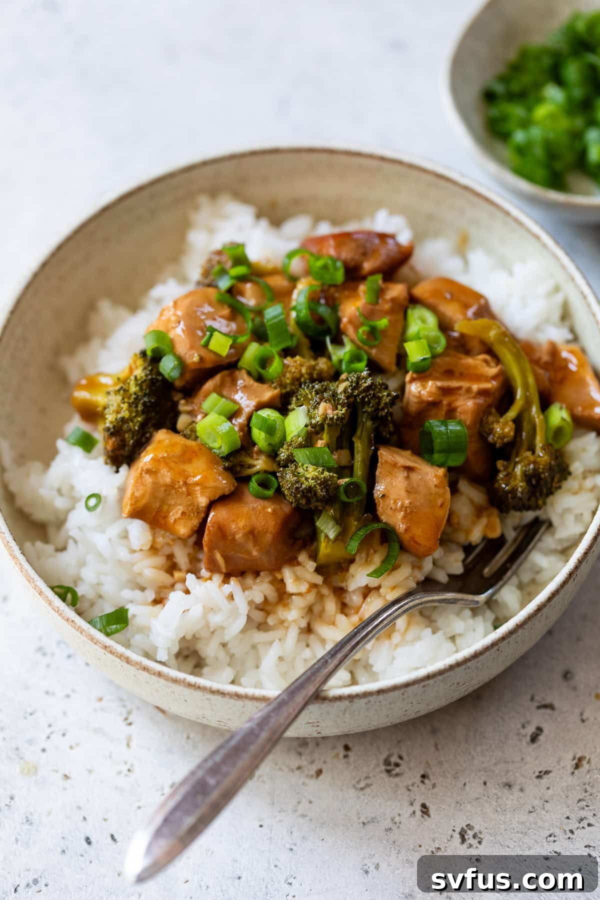 A bowl of delicious Slow Cooker Orange Chicken served with fluffy white rice and steamed broccoli, garnished with fresh green onions.