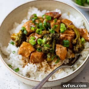 A bowl of delicious Slow Cooker Orange Chicken served with fluffy white rice and steamed broccoli.