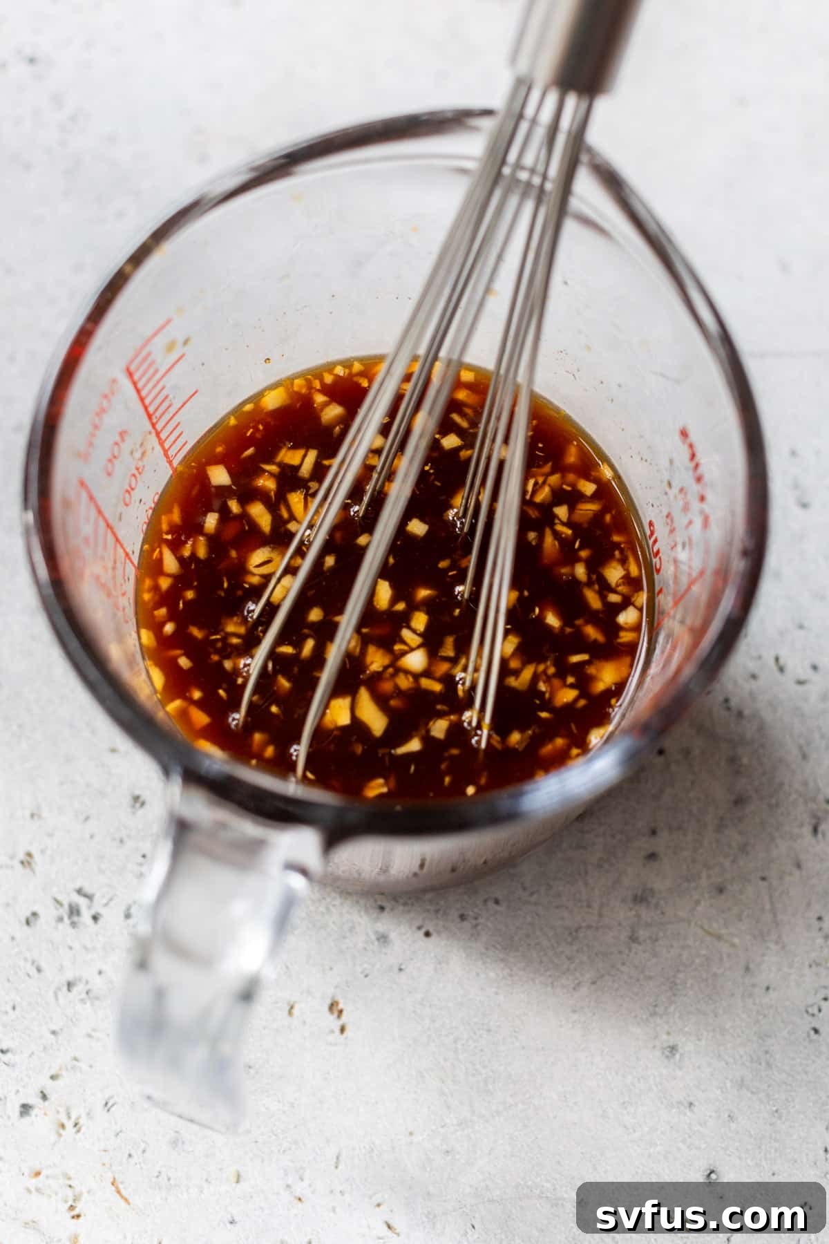 A hand whisking together orange sauce ingredients in a clear glass measuring cup.