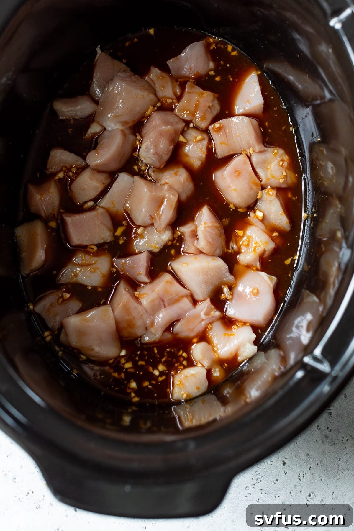 Raw diced chicken pieces covered in orange sauce, ready for slow cooking.
